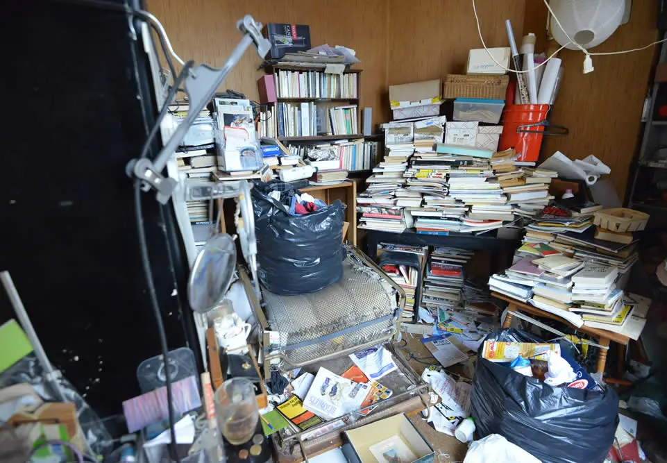 Bureau encombré de livres, cartons et sacs nécessitant un débarras